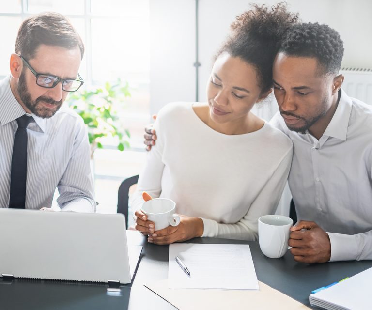 Man and Women with coffee cups in hands, looking over another man's laptop.